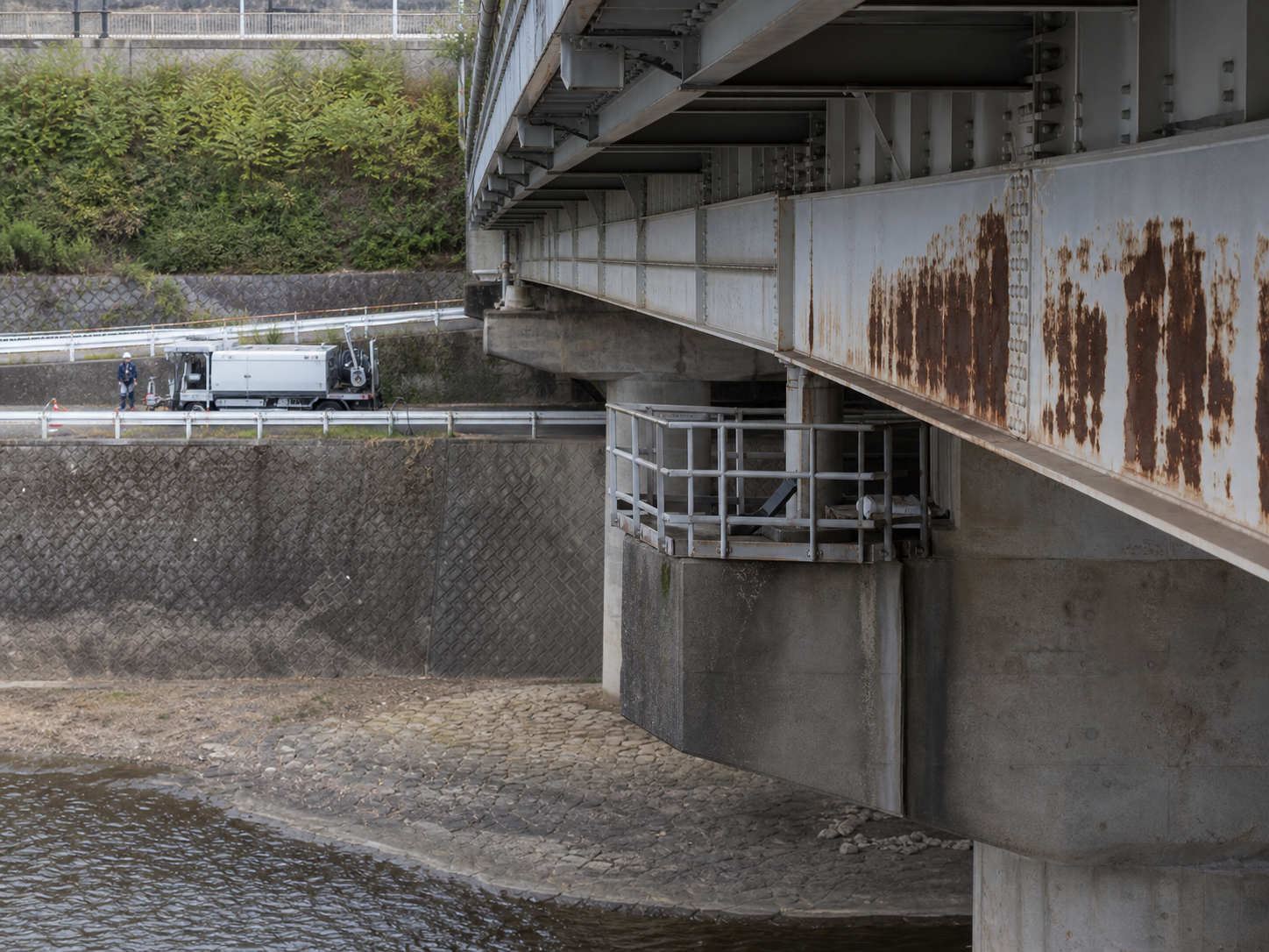 大型装置が橋梁の錆除去対象部位へ近づけない現場制約を示す写真調ビジュアル